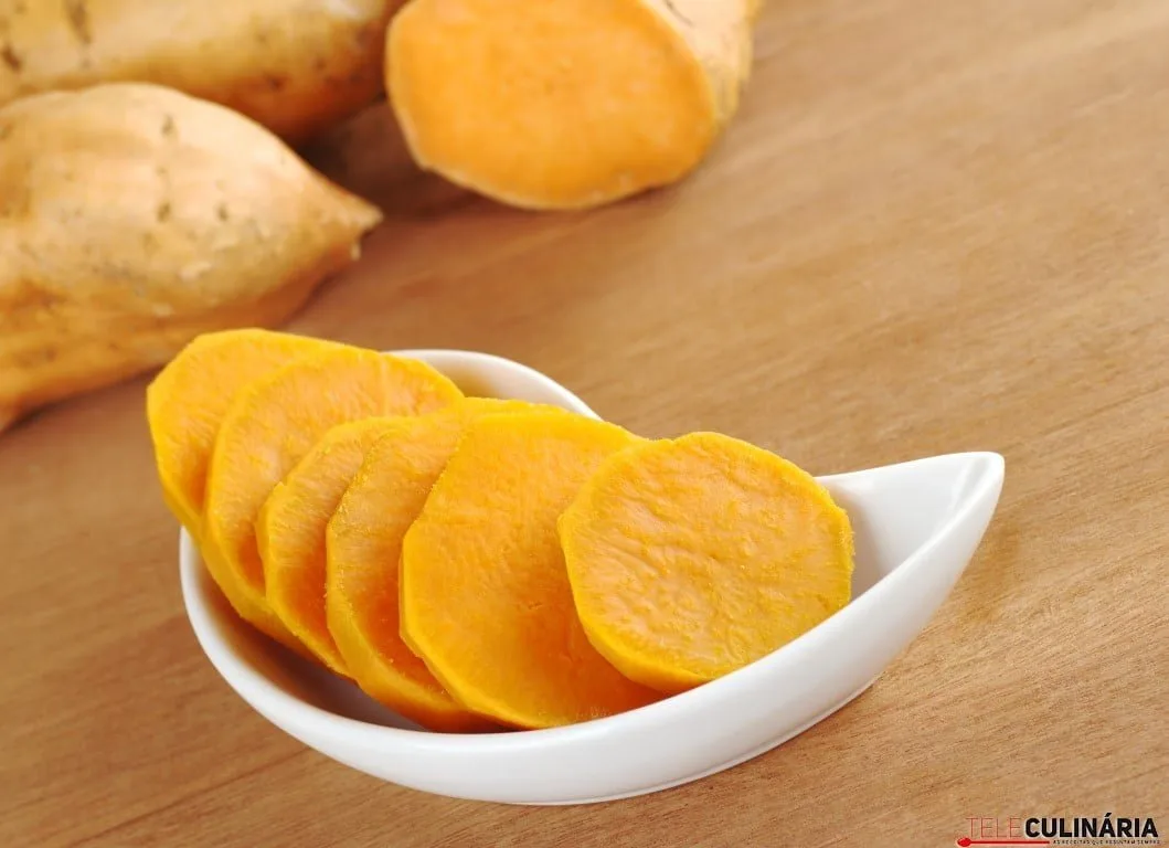Cooked sweet potato (lat. Ipomoea batatas) cut in slices in white bowl on wooden surface with sweet potatoes in the background (Selective Focus, Focus on the sweet potato in the bowl)